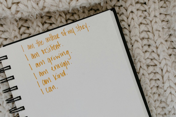 A close-up of an open notebook with handwritten affirmations on a cozy knitted background.